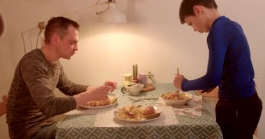 Bir adam ve bir çocuk bir masada oturmuş lezzetli bir yemeğin tadını çıkarıyor, kahkaha ve besinlerle dolu bir anı paylaşıyorlar.