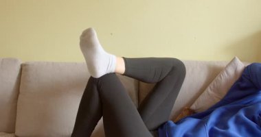 Videoda bir kadın kanepeye uzanmış beyaz çoraplarını giyip eğlencesine bacak bacak üstüne atıyor, rahat bir ortam yaratıyor.