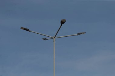 Üzerine üç parlak ışık monte edilmiş uzun bir sokak lambası güzel mavi bir gökyüzü zeminine karşı kurulmuş.