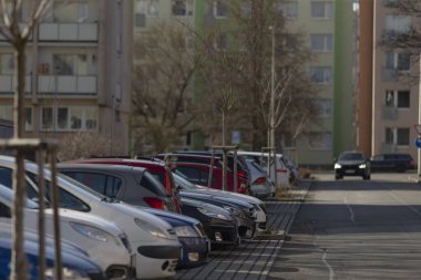 Büyük bir binanın önündeki otoparkta, düzgün park edilmiş ve düzenlenmiş bir sıra araba görülebilir.