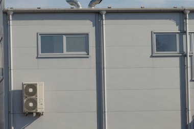 İki penceresi olan gri bir bina var ve binanın yan tarafına monte edilmiş bir klima var.