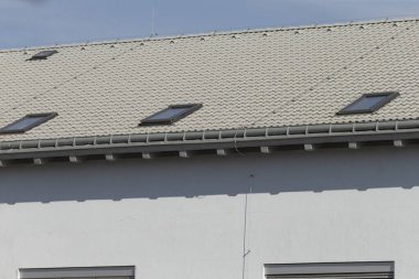 Beyaz bir bina, el değmemiş beyaz bir çatı, iki çatı penceresi ile tamamlanmış, iç mekâna doğal ışık katıyor.