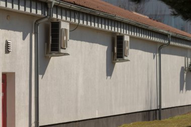 Havalandırma kontrol amacıyla yan tarafına yerleştirilmiş iki havalandırma ünitesi bulunan önemli bir beyaz bina var.