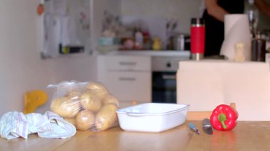 Geniş bir mutfakta taze patatesler, canlı bir dolma biber ve temel mutfak gereçleri bulunur.