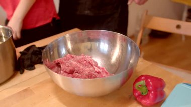 Kırsal bir ahşap masada, bir kase baharatlı öğütülmüş etle dolu ve yanında canlı kırmızı bir dolma biber var.