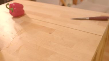 Yanında parlak kırmızı bir çan biberi ve keskin bir mutfak bıçağı olan renkli bir doğrama tahtası.