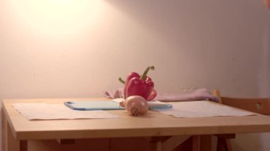 Sıcak ışık altında, ahşap bir masada parlak dolmalık biberler, rahat bir ev mutfağı havası sergiliyor.