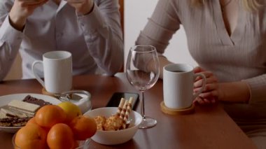 Sıcak bir masadaki iki insan kahve, atıştırmalıklar ve portakal gibi taze meyvelerin tadını çıkarırlar.