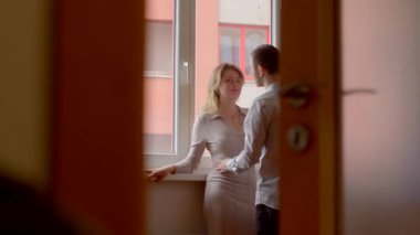 İki birey, pencerenin kenarında, arka planı bulanık ve rahat bir şekilde sohbet ediyorlar.