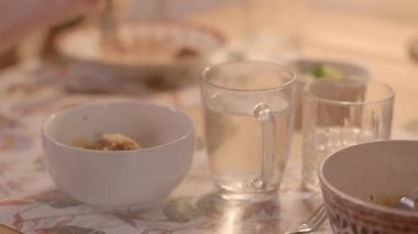 Video, çeşitli yemek kaseleri ve su bardaklarıyla dolu bir yemek masasının altını çiziyor. Su dolduran bir insanın görüntüsü, davetkar yemek atmosferini arttırıyor.