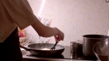 Bir birey mutfakta yemek pişirmeye odaklanır, kızartma tavasında çeşitli malzemeleri ustalıkla hazırlar.