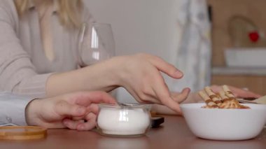 Sıcak bir mutfakta, bir kadın mısır gevreğini canlı bir meyve tabağının üzerinde tutarken, bir çift de yemek ve şarap içerek, el ele tutuşarak sıcak bir konuşma yapıyor.