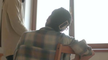 Pencere arkası olan bir odada, iki birey bir sohbete dahil oluyor, anlamlı bir şekilde etkileşime geçiyorlar.