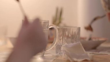 Bir yemek masasında sahneyi canlandıran temiz su bardakları, bir el ve yumuşak arkaplan elementleri bulunur.