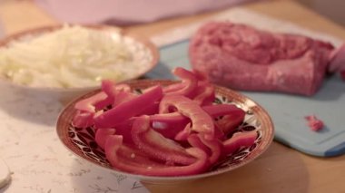 Mutfak tezgahında, yanında biraz çiğ etle birlikte dilimlenmiş kırmızı dolmalık biber görebilirsiniz.