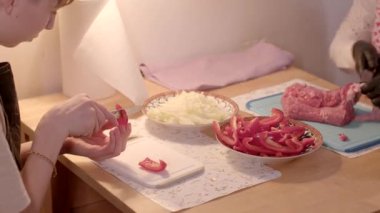 Becerikli bir aşçı mutfak masasında kırmızı bir dolma biberi doğruyor. Yanında doğranmış soğan ve et var.