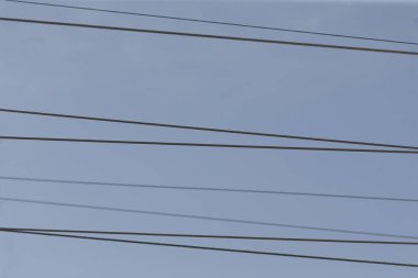 Gökyüzü boyunca uzanan uzun bir elektrik hattı, yukarıdaki parlak mavi arkaplana karşı canlı bir tezat oluşturarak, elektrik şebekelerini sembolize ediyor.