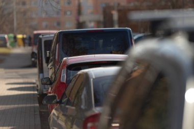 Yolun kenarında düzgün bir şekilde park edilmiş uzun bir sıra araba yer kaplıyor ve farklı renkler ve stiller sergiliyor.