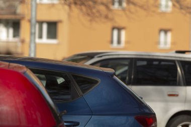 Geniş bir otoparkta, parlak kırmızı bir araba parlak mavi bir arabanın yanına park edilir, seyircilerin hayran olacağı renkli bir sahne yaratır.