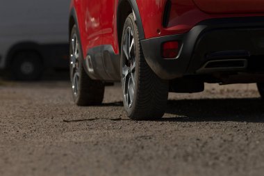 Yoğun yolun kenarına park etmiş canlı kırmızı bir araba arka planda çarpıcı bir görüntü yaratıyor.