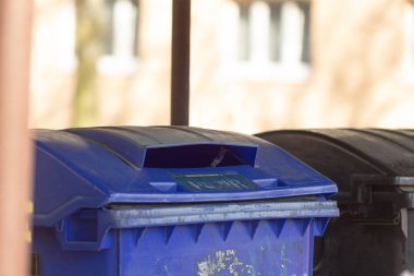 Canlı bir mavi çöp kutusu şu anda parlak siyah bir çöp tenekesinin yanına yerleştirilmiş ve yan yana ilginç bir kontrastlık oluşturuyor.