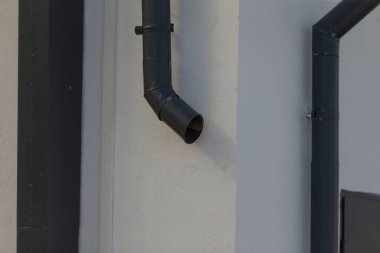 Bu resim, el değmemiş beyaz bir duvara monte edilmiş parlak siyah bir oluğun detaylı bir yakın plan görüntüsünü sergiliyor.