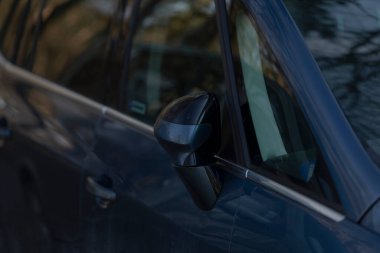 Bu resim mavi bir otomobile ait yan aynanın detaylı bir yakın görüntüsünü gösteriyor. Çeşitli özellikleri vurgular