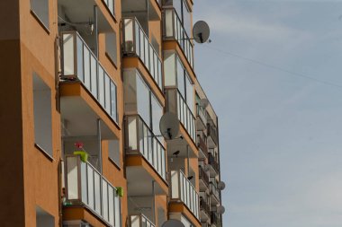 Yüksek bir binanın dış yüzeyinde çok sayıda balkon ve birkaç uydu anteni bulunur ve yerleşim yeri oluşturur.