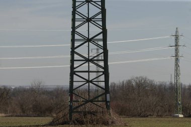 Geniş bir alanın ortasında çeşitli yönlere doğru uzanan birkaç üstten elektrik hatlarıyla çevrili büyük metal bir kule bulunur.