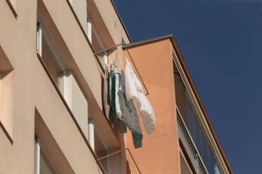 Giysiler binanın dışında asılı duran bir çamaşır ipine asılıyor ve çevresine renkli bir dokunuş katıyor.