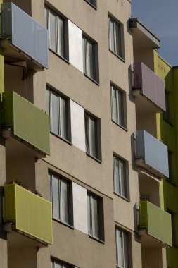 Çok sayıda pencere ve birkaç balkona sahip yüksek ve geniş bir bina, kentsel ufuk çizgisinde göze çarpıyor.