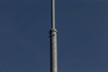 Uzun bir metal direk belirgin bir şekilde açık mavi gökyüzüne karşı duruyor, parlak şekli ve güçlü varlığıyla çarpıcı bir görüntü yaratıyor.