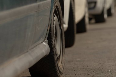 Bu resim, arka planda birkaç park etmiş aracın görüldüğü patlak bir lastiğin yakın görüntüsünü içeriyor.