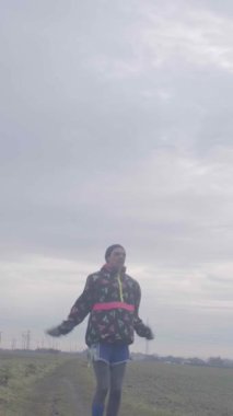 Bir birey engin bir kırsal alanda dar bir yolda yürüyor ve yanında bulutlu bir gökyüzü var.