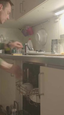 Bir birey, yumuşak ve sıcak aydınlatma altında çeşitli tabakları bir mutfak dolabına dikkatlice yüklüyor.