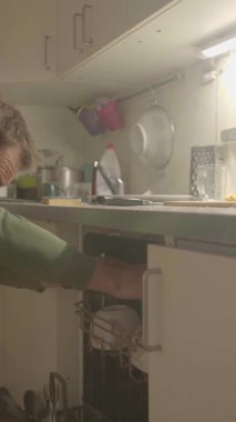 Bir insan, mutfak ortamında bulaşık makinesine çeşitli bulaşıkları dikkatlice yerleştiriyor.