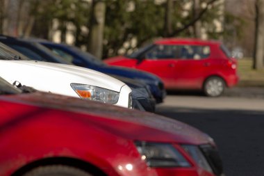 Bir otoparkta, arka planda çoğunlukla kırmızı ve beyaz araçlar olmak üzere çeşitli arabalar mevcuttur.