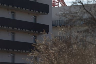 Çevresinde ağaçlar bulunan kentsel yapı cephesi, arka planda inşaat elementleri sunuyor