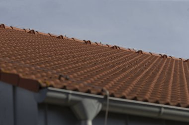 Bu resim, çarpıcı kırmızı kiremitli çatının detaylı bir yakın çekimini gösteriyor. Mükemmel bir zemin görevi gören canlı mavi gökyüzüne karşı kurulmuş.