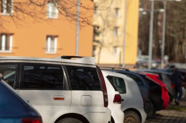 Şu anda büyük bir binanın önündeki geniş bir otoparkta uzun bir sıra araba duruyor.