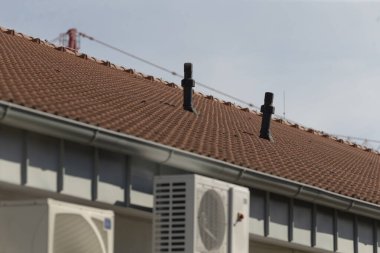 Havalandırmayla süslenmiş bir çatı ve temiz, mavi bir gökyüzünün arka planına karşı bir klima görünür.