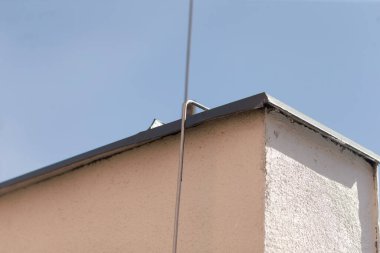 Bir çatının kenarı, güzel, berrak bir gökyüzü arka planına belirgin bir şekilde kurulmuş bir anten içerir.