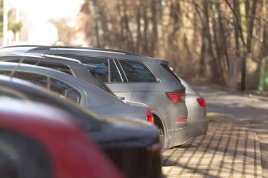 Arabalar düzgünce sokağın bir tarafına park edilmiş, arka planda bulanık ağaçlar huzur yaratıyor.