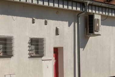 Güvenlik amacıyla üzerine metal parmaklıklar takılmış pencerenin yanında parlak kırmızı bir kapı bulunan beyaz bir bina.