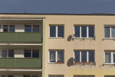 Açık mavi gökyüzünün altında, balkonları ve uydu anteni olan çok katlı bir apartman.