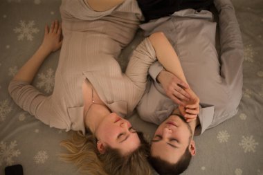 Bir çift, birbirine yakın bir anı paylaşan, desenli bir arka planda yan yana dinleniyor.