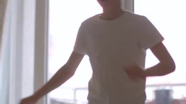Bu video beyaz tişörtlü, neşeli bir gencin parlak bir oturma odasında neşeli aktivitelere girişini, neşe ve enerjiyi görüntülemesini içeriyor.