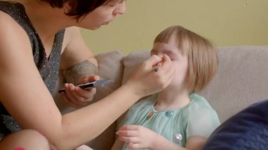 Kapalı bir mekanda bir anne, genç kızına sevgiyle makyaj yapar. Bu paylaşılan deneyimde yaratıcılık ve şefkat dolu samimi bağlarının altını çizer.