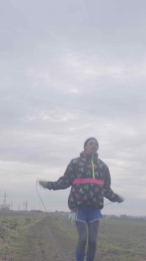 Atletik giyinmiş bir şahıs bulutlu bir gökyüzünün arka planında dikiliyor.