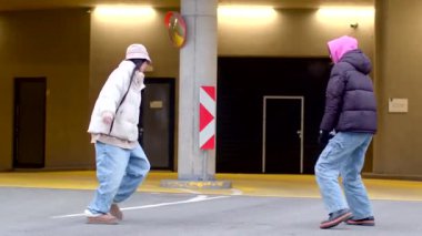 Park yeri içeren şehir ortamında dinamik dans hareketleri yapan iki kişi.